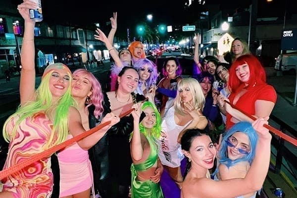 Partygoers in colorful wigs and costumes riding the open-air party bus at night